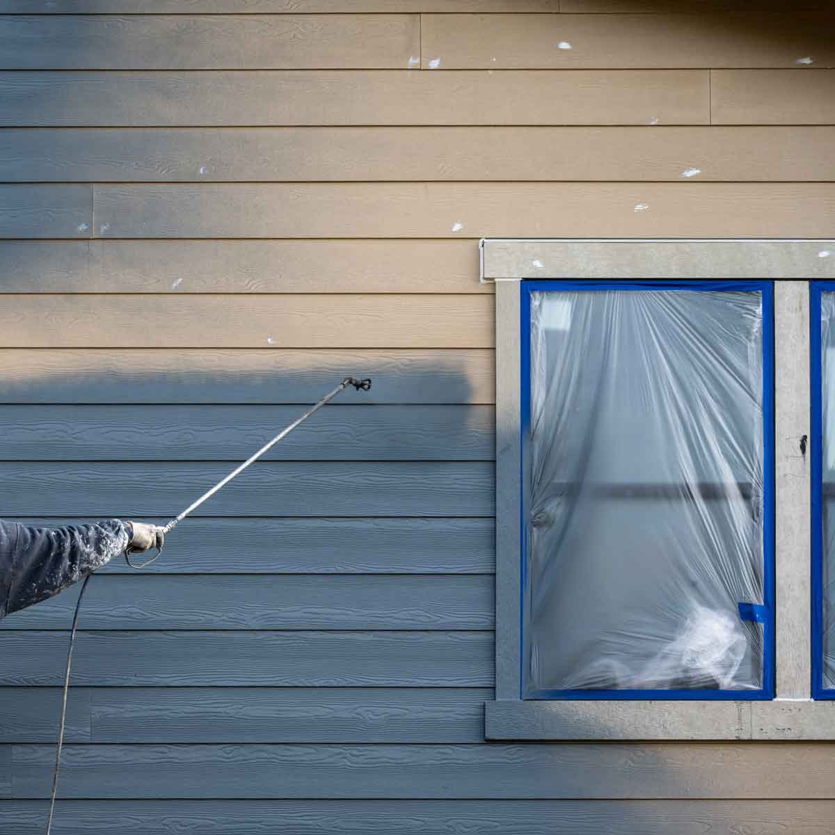 Person painting siding with paint sprayer